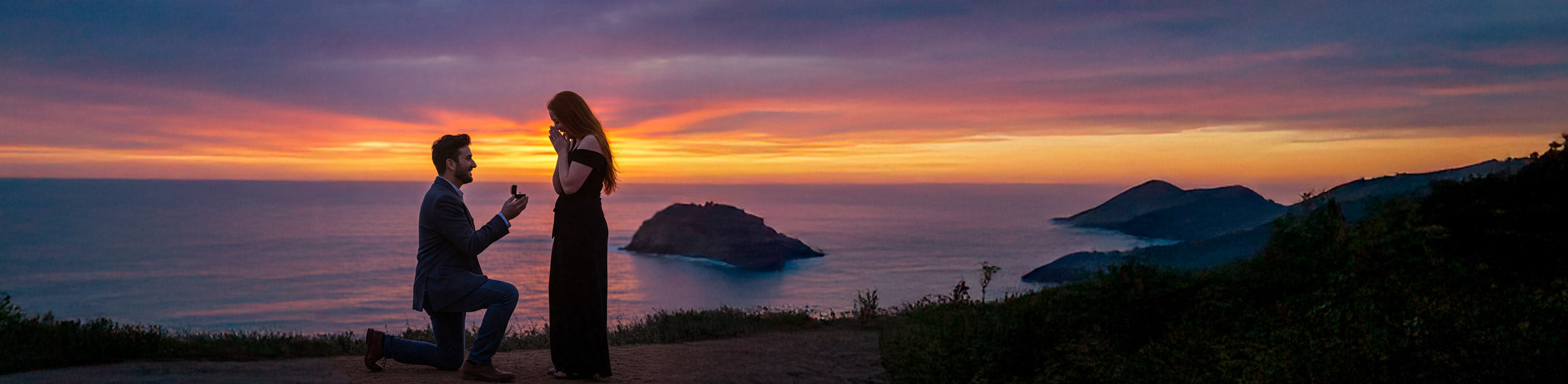 Man proposing to a woman on a cliff overlooking the ocean at sunset.