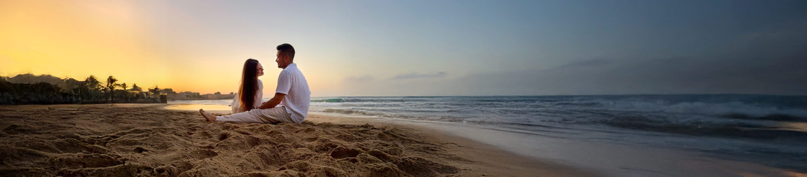 Couple sitting on a beach at sunset with ocean waves in the background